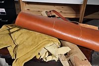 Smooth brown leather piece with two sewn leather straps laid over tan suede leather scraps on a surface.