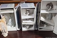 Three boxed Lladro figurines showing different young girls in pastel dresses and floral bases with protective foam inserts. Gentle Spirit statue visible on left.