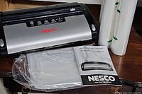 Nesco vacuum sealer with instruction manual and two vacuum sealer bags next to it