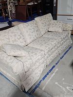 Full view of the skirted sofa with branch pattern upholstery showing the overall condition and design of the piece with cushions in place.