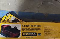 Box packaging with image and branding highlighting the EZ Roll Tonneau cover fitted on a red truck bed.