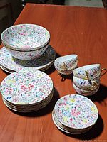 Wide angled photo showing the whole lot arranged on a table: plates, large bowls and tea cups with a floral pattern.