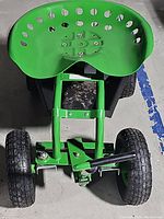 Close-up view of the green tractor-style perforated metal seat and front axle with four pneumatic tires.