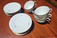 Overall view of eight cups stacked beside eight saucers on a wood surface