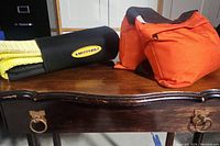 Black neoprene Smittybilt winch tree protector and one orange rope weight on wood table