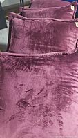 Four plum colored velvety UGG throw pillows arranged on a surface showing texture details.