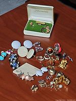 Top view of assorted vintage earrings displayed on a table with a Krementz box containing floral clip-ons and hoop earrings.
