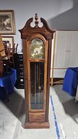 Full view of the tall wooden grandfather clock with glass front showing pendulum inside.