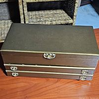 Closed view of rectangular gold-tone jewelry box with two drawers and top handle on a wooden surface.