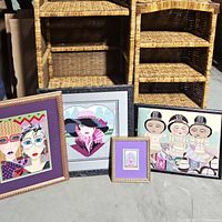 Four framed needlepoint artworks placed in front of woven shelves. Two have gold frames and two have black frames.