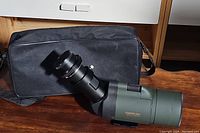 Visionking spotting scope laying next to soft black carrying case on wood surface.