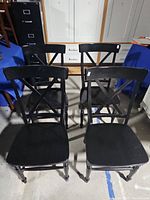 Four black wooden dining chairs with X-back design viewed from above.