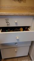White kitchen drawers with round knobs partially open showing contents inside for kitchen utensil lot