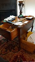 Full view of wooden side table showing one drawer open, scratches visible on surface, holding remotes and papers.