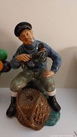 Front view of Royal Doulton 'The Lobster Man' figurine depicting a fisherman holding a lobster and net, seated on a rock.