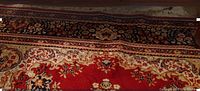 Photo shows a close-up of the red oriental-style area rug with intricate floral and medallion designs in black, beige, and other accent colors, highlighting the pattern and condition.