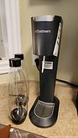 Front view of black SodaStream carbonation machine with two clear bottles on left side, placed on kitchen counter.