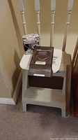 Photo of plastic step stool with hobby box, hair clipper box and trivia mug on top