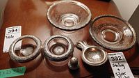 Photo of two silver plate trimmed glass bowls, two small salt bowls with silver plate rims, silver tea strainer, and sterling salt shaker on wood surface.