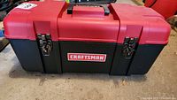 Closed Craftsman plastic toolbox with black base and red lid, metal latches, and central handle