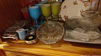 Wide view of assorted glass serving plates, plastic drinkware in various colors, small ceramic pitcher, floral plates, and glass bowl vase