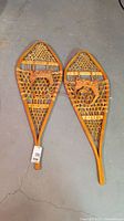 Pair of vintage wooden snow shoes laying on a concrete floor, showing the top side and the webbing detail.