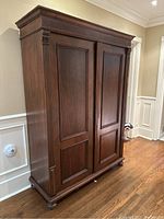 Front right three-quarter view of walnut armoire showing doors, crown molding, bun feet