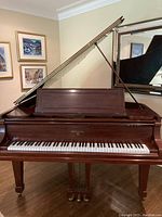 Front view of piano with lid propped open above music desk, fallboard retracted to expose keys