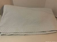 Folded pale blue coverlet showing diamond quilted pattern and edges.