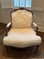Front view of armchair showing carved crest, loose back cushion, seat cushion and upholstered arms.
