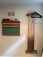 Full view showing oak scoreboard, rack with five cues and triangle, plus brush on top of scoreboard