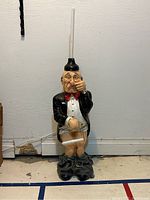 Full view of humorous bathroom figurine lawyer with plunger on his head and pants down holding toilet paper holder.