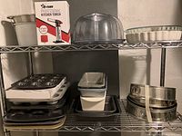 Wide shot showing shelving with multiple baking items including metal pans, muffin tins, bundt pans stacked, and plastic bundt cake dome.