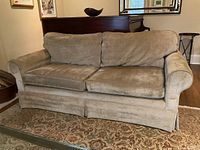 Front view of dark taupe velvet two-seater sofa with rolled arms and tailored skirt.