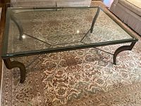 Front perspective of full coffee table showing glass top and metal base on patterned rug