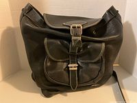 Front view of black pebbled leather Roots backpack satchel showing the flap and front buckle pocket.