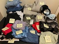Photo showing folded tops, cardigans, skirts, pants, and accessories with sticky notes labeling each item and size details.