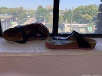 Side and top view of the black Birkenstock thong sandals with pink soles on a ledge by a window.