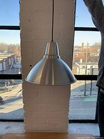 Side view of the large metal industrial hanging lamp in brushed steel finish, suspended by a black cord.