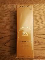 Front view of the gold-colored Lancome Paris Self Tan Flash Bronzer sealed packaging showing product name and volume.