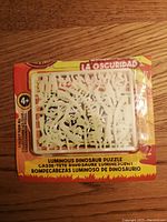 Front packaging showing glow-in-the-dark dinosaur bone pieces in plastic sprue frame inside orange packaging.