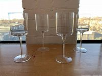 Four clear wine glasses shown on wooden surface with a window and brick wall background.