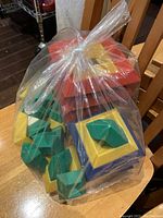 Plastic stacking blocks and pyramid pieces inside a clear plastic bag on a wooden chair
