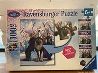 Front of the Ravensburger box showing the Disney Frozen puzzle image with characters Olaf, Sven, Elsa, and Anna, marked 100 XXL pieces, recommended for ages 6+