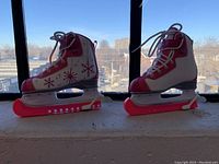 Side view showing both skates upright on window sill with pink blade guards attached.