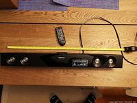 Top view of the Samsung soundbar with a yellow measuring tape extended along its length and a remote control placed on top.