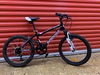 Side profile of the Supercycle Impulse children's bicycle showing black and white frame, knobby tires, seat, and pedals.
