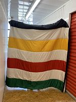 Full view of the sleeping bag held up, showing green, red, yellow, and white wide horizontal stripes with dark edges.