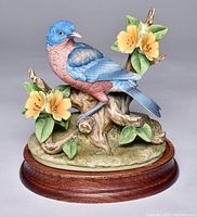 Front view of the detailed bluebird figurine on wood base showing the bluebird, tree stump, yellow flowers, and leaves.