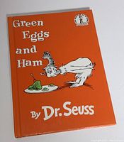 Front cover of Dr. Seuss Green Eggs and Ham hardcover book with orange background and illustration of Sam-I-Am with a plate of green eggs and ham.